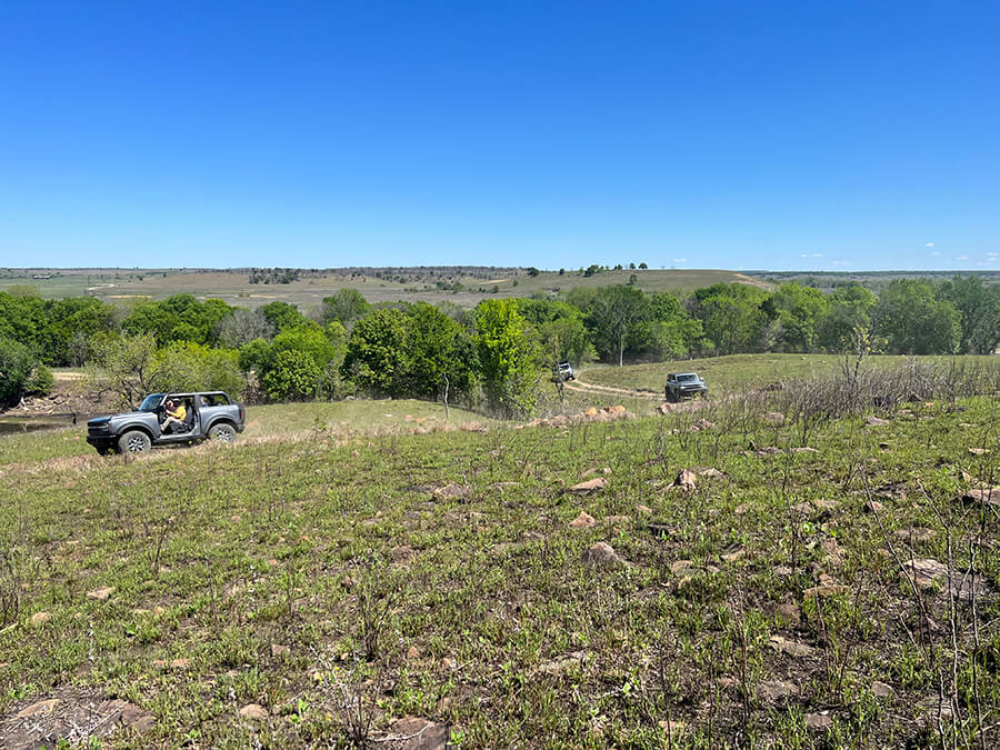A view of a Ford Bronco driving on a dirt road from a distance.