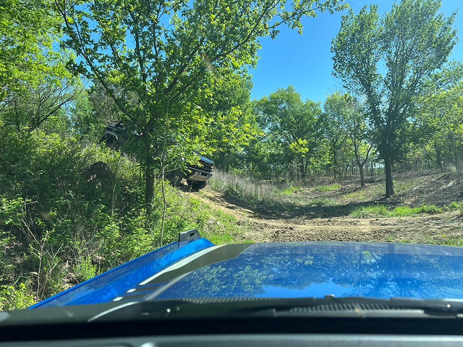 A view of a blue Ford Bronco's interior while off-roading in a forest.