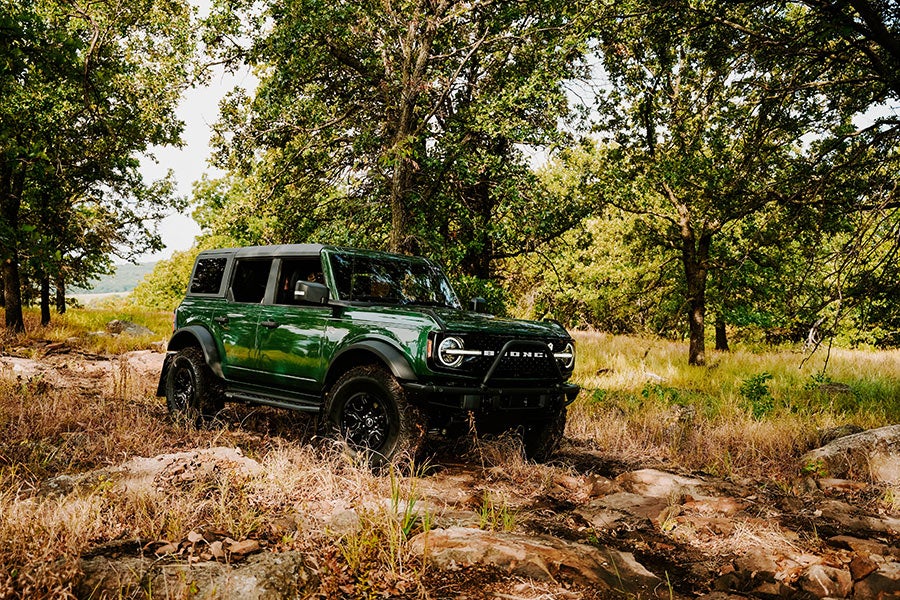 A green Ford Bronco parked on a rocky off-road trail