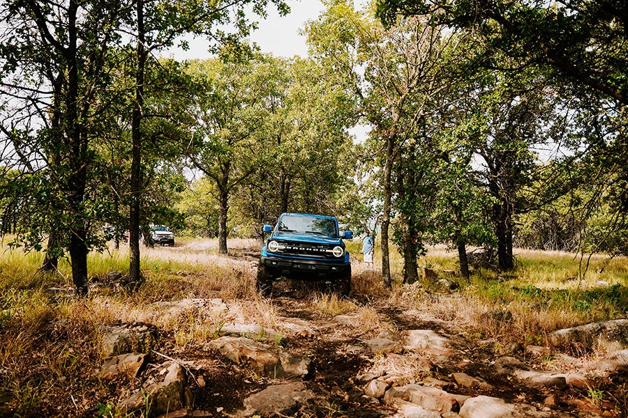  A blue Ford Bronco driving on a dirt road in a forest