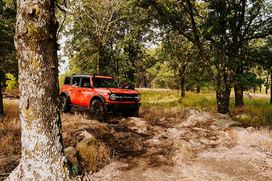 An orange Ford Bronco parked on a trail in the woods