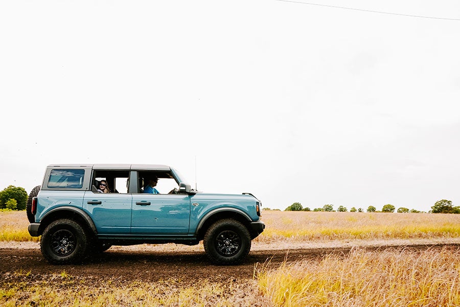 A light blue Ford Bronco parked on a dirt road in a field