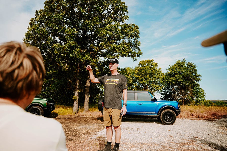 A person standing next to a blue Ford Bronco outdoors