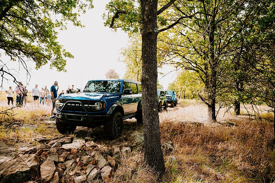 A blue Ford Bronco driving on a dirt road in a forest