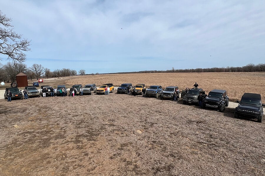 A long line of Ford Broncos parked in a large field