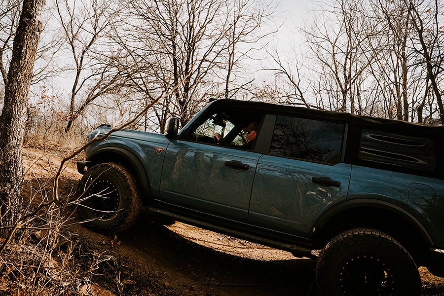 A side view of a green Ford Bronco off-roading on a hill.