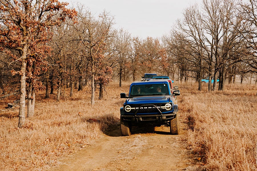A front view of a blue Ford Bronco driving on a dirt road.
