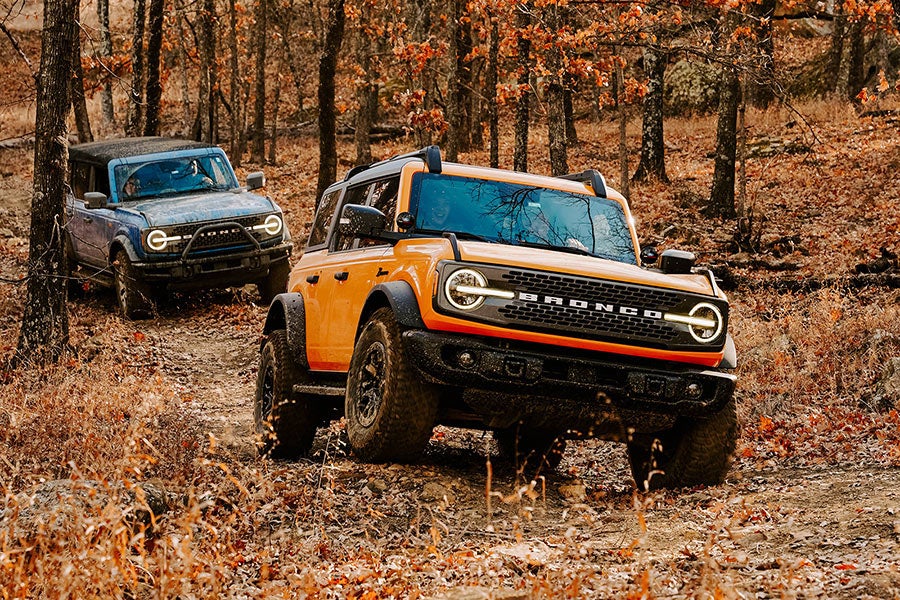 A side view of a yellow Ford Bronco off-roading on a rocky trail.