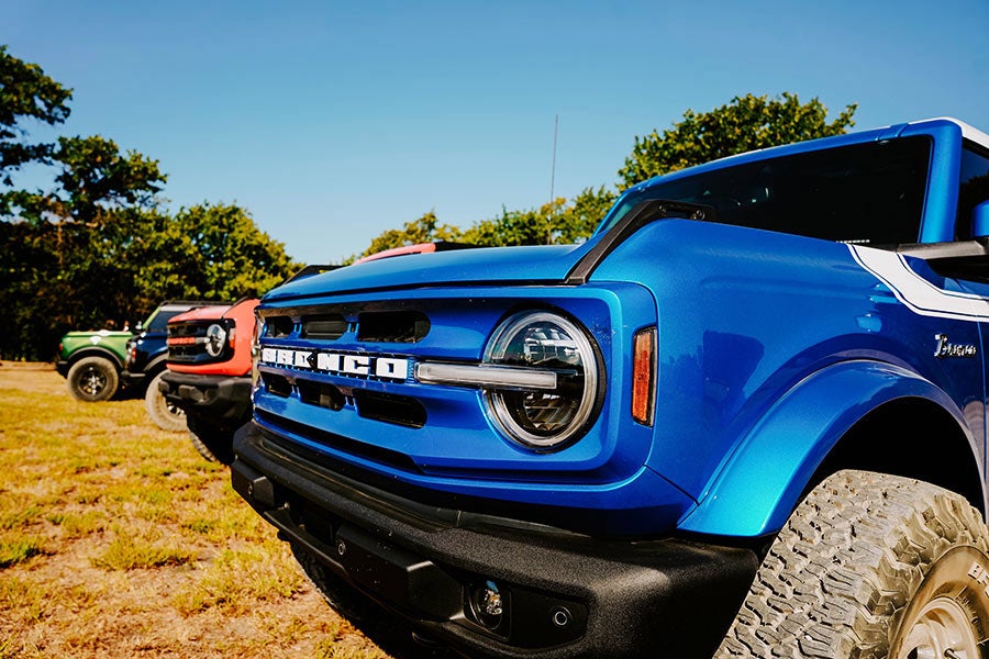 A close-up side view of a blue Ford Bronco's grille and headlights.