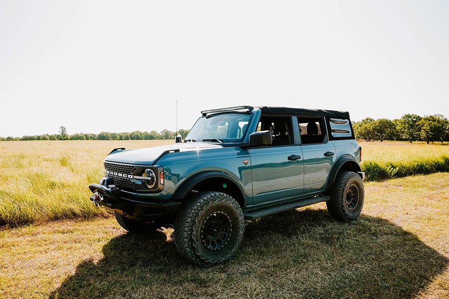 A side view of a red Ford Bronco off-roading with a tilted front tire.