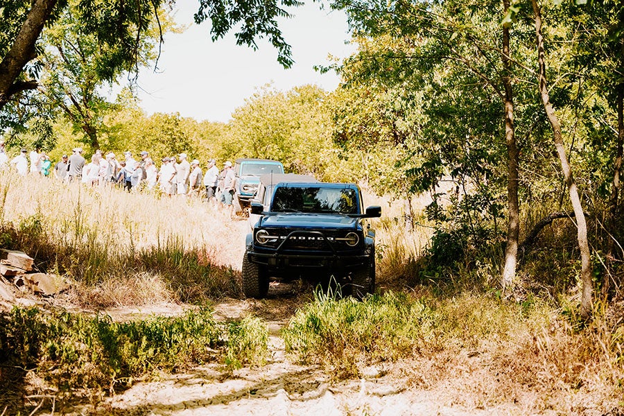 A side view of a gray Ford Bronco off-roading on a dirt trail.