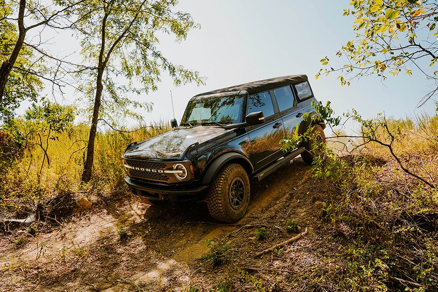 A side view of a dark Ford Bronco off-roading.