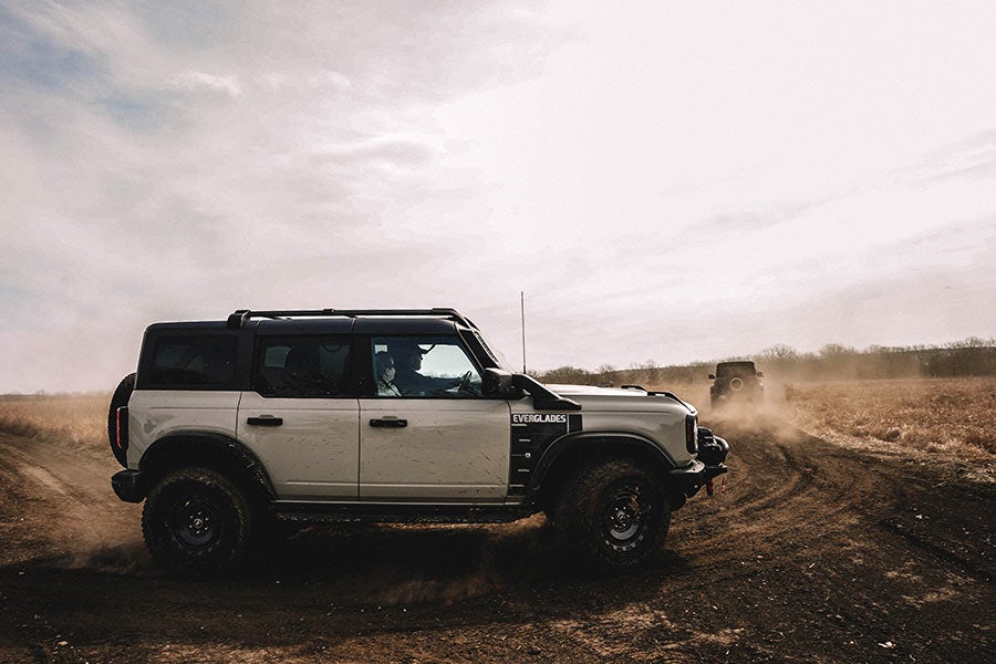 A front view of a blue Ford Bronco driving on a dirt road.