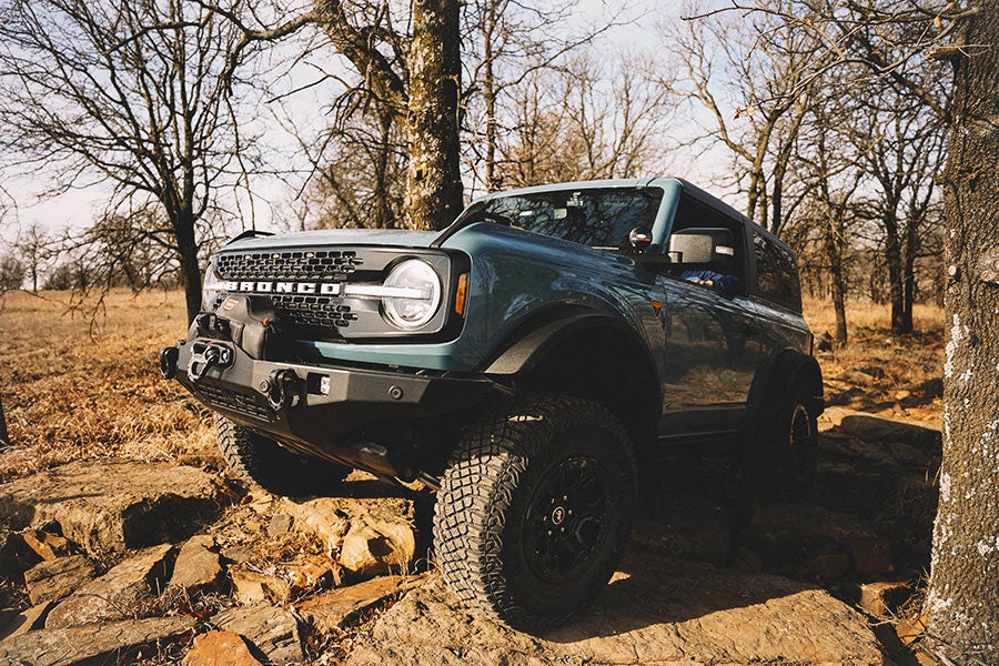 A side view of a dark Ford Bronco with a tilted front tire.