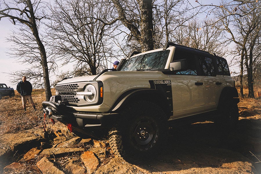 A side view of a green Ford Bronco off-roading with a tilted rear tire.