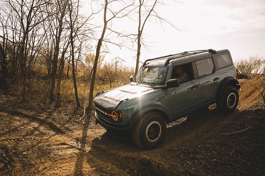 A side view of a silver Ford Bronco off-roading.