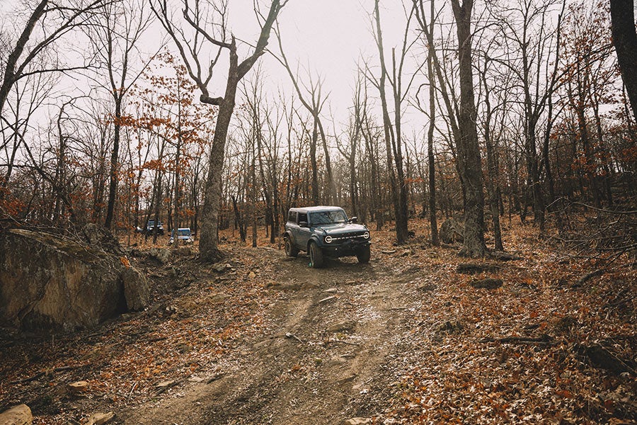 A front view of a black Ford Bronco driving on a dirt trail.
