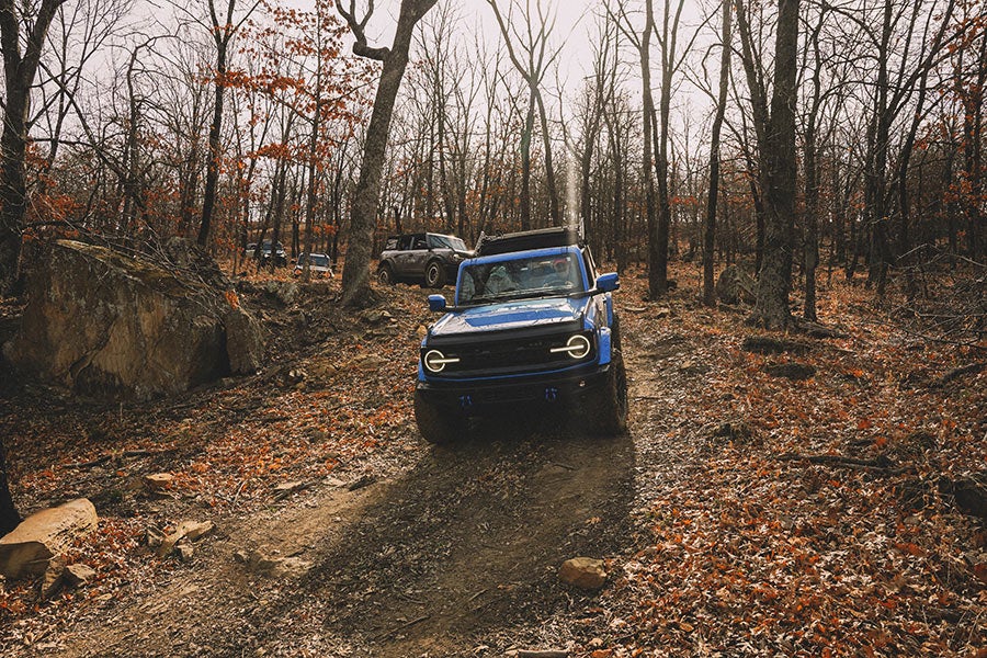 A front view of a black Ford Bronco with its lights on.