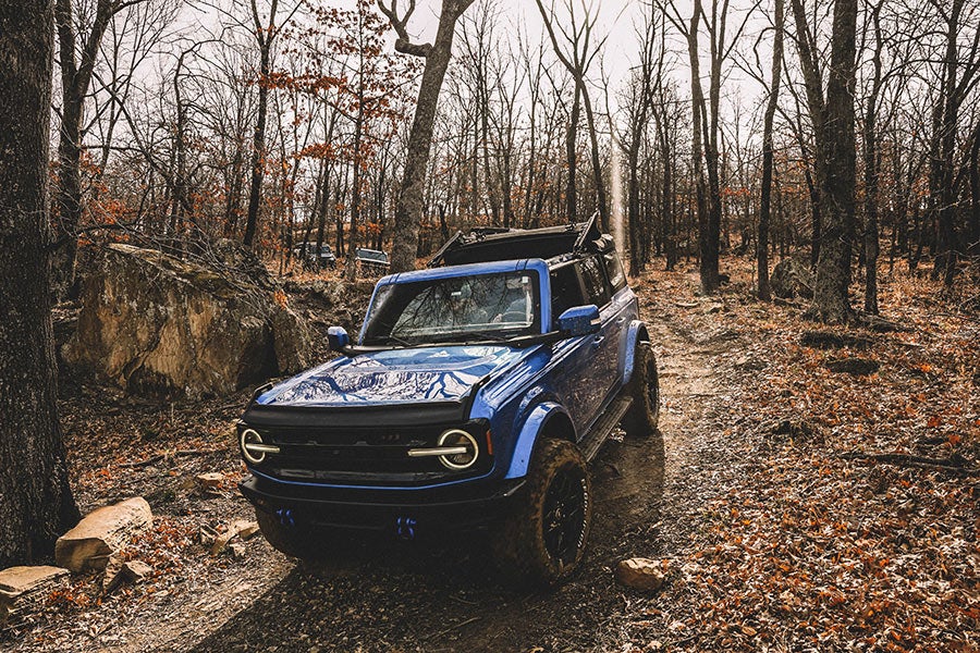 A front view of a blue Ford Bronco with its lights on.