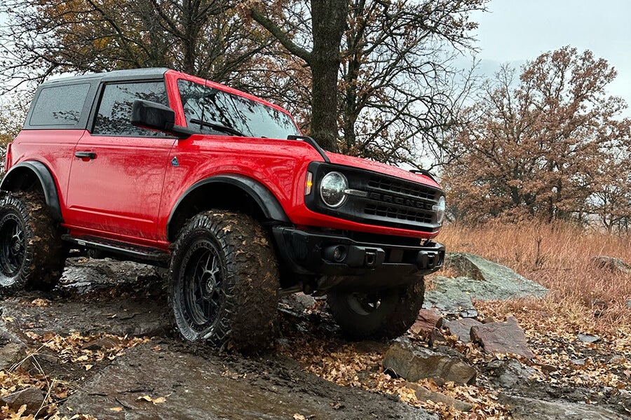A red Ford Bronco driving on a muddy, rocky path.