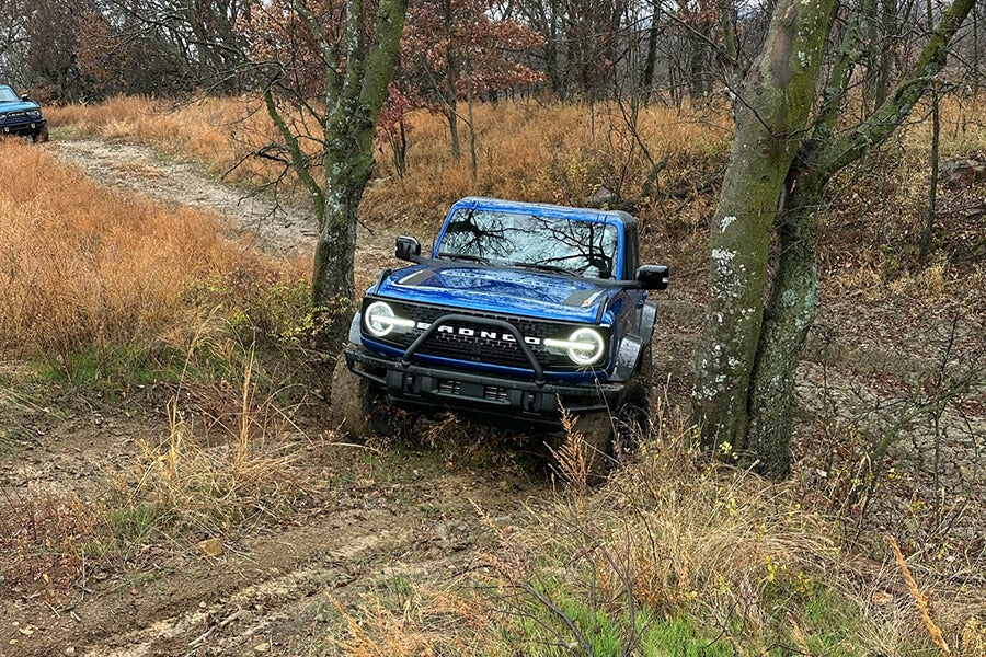  blue Ford Bronco driving on a dirt road in a field.