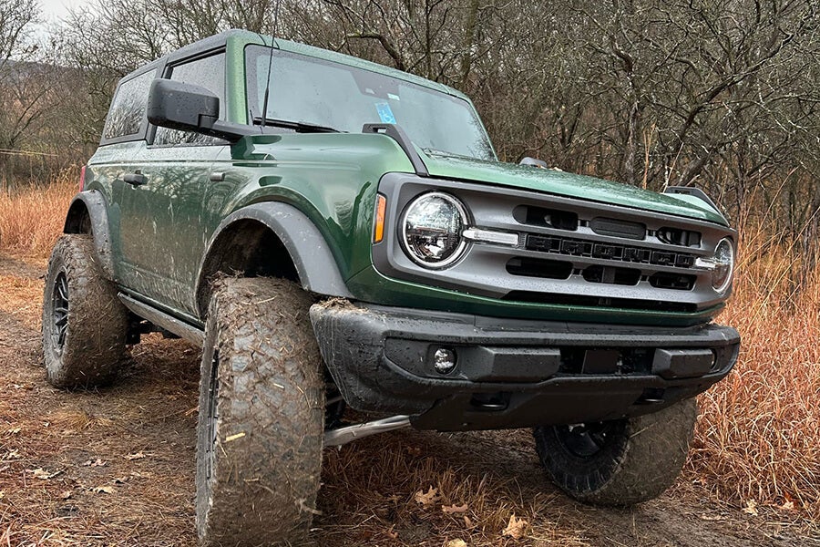 A green Ford Bronco parked on a muddy trail in the woods.