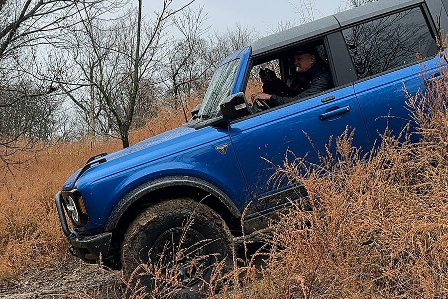 A blue Ford Bronco driving on an incline on a dirt road.