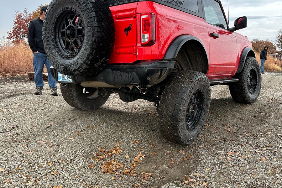 A red Ford Bronco with a raised rear tire on an off-road trail.