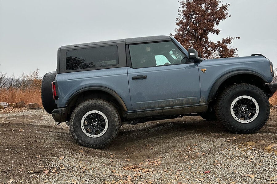 A light gray Ford Bronco parked on an incline on a dirt road.