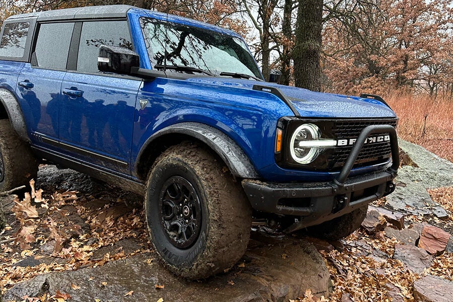 A close-up of a blue Ford Bronco driving on a muddy trail.