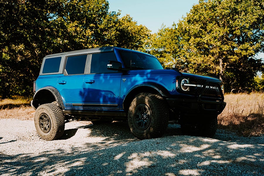 A blue Ford Bronco is parked on a gravel path outdoors
