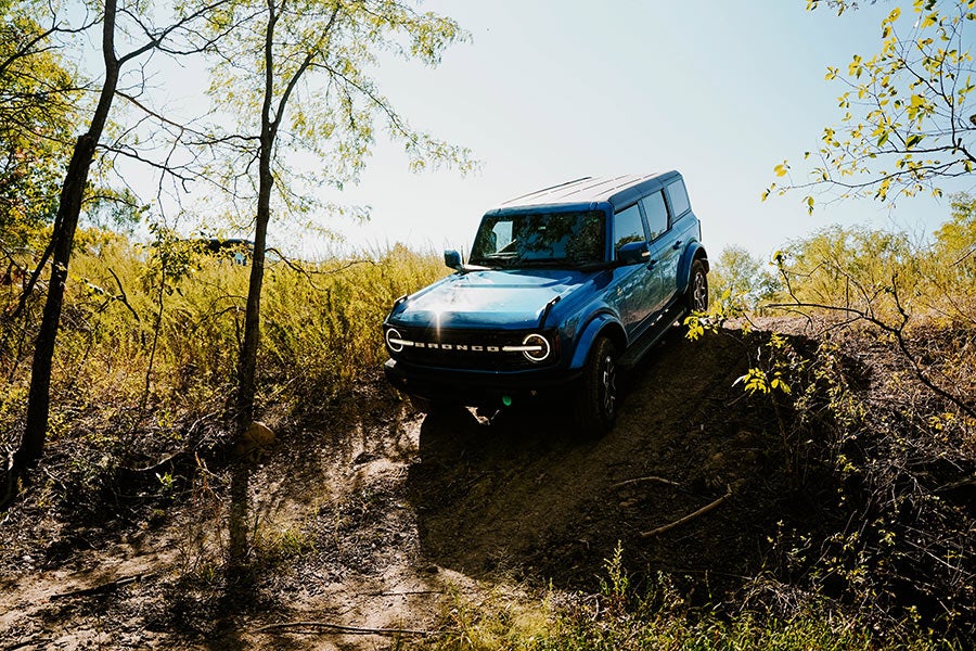 A blue Ford Bronco driving on a dirt road in a forest.