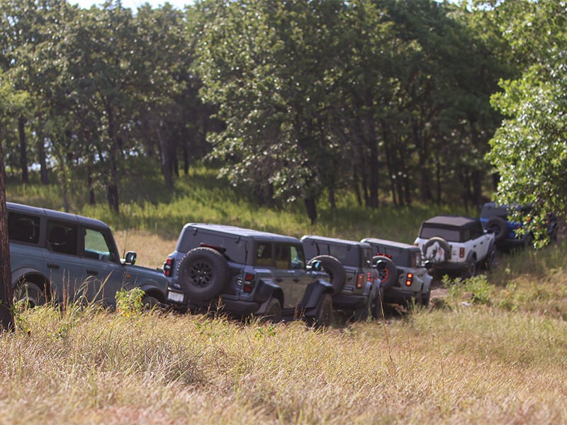 A line of off-road vehicles driving on a dirt path next to a field