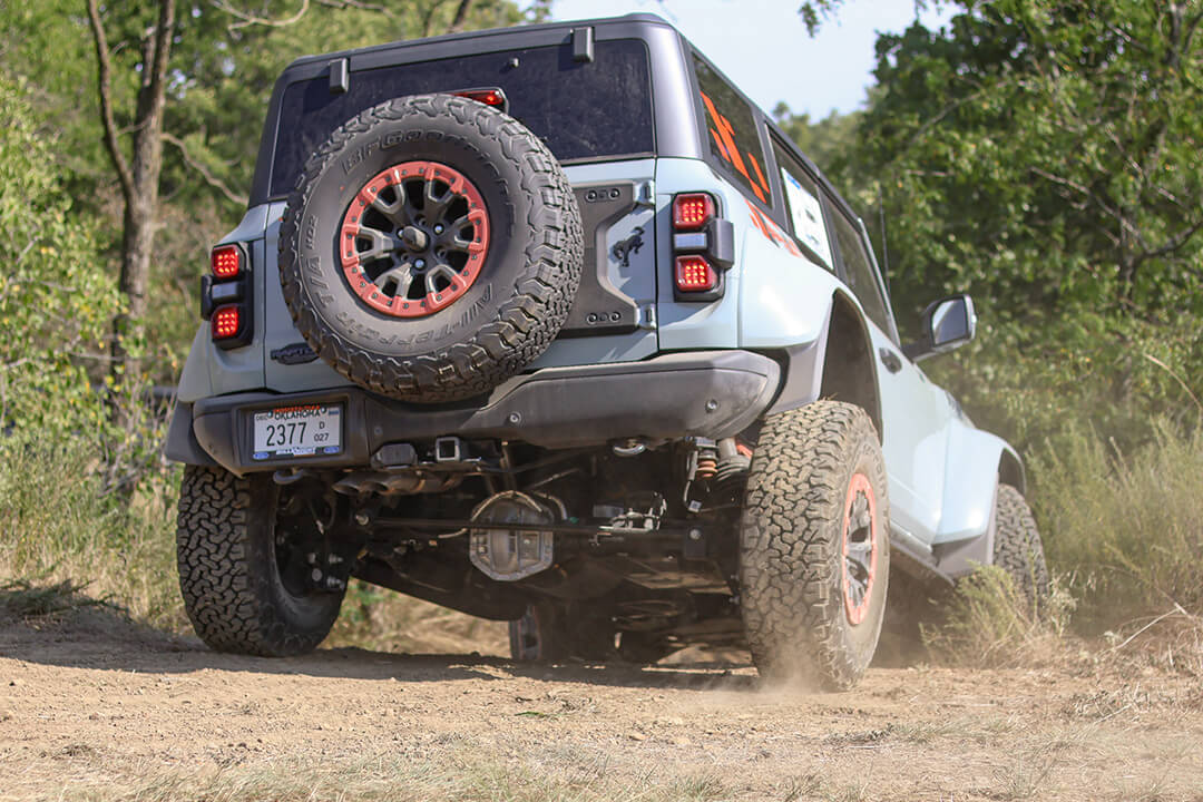 A rear view of a Ford Bronco with its rear tire on a large rock.