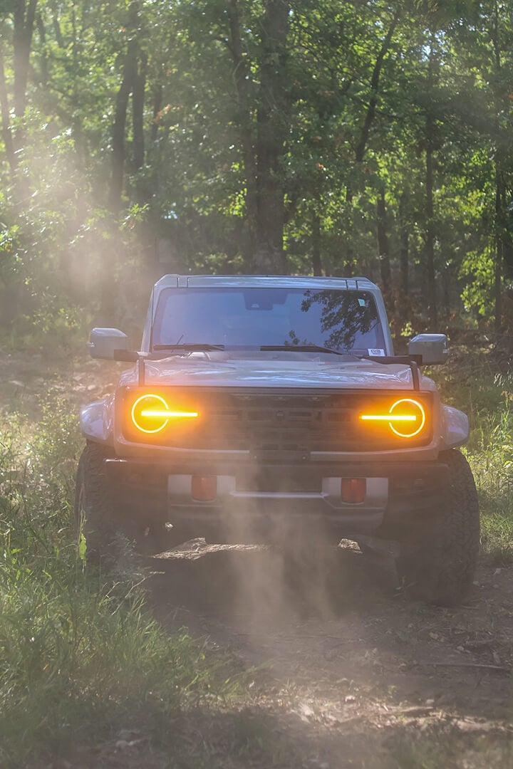 A front view of a Ford Bronco with its lights on at night