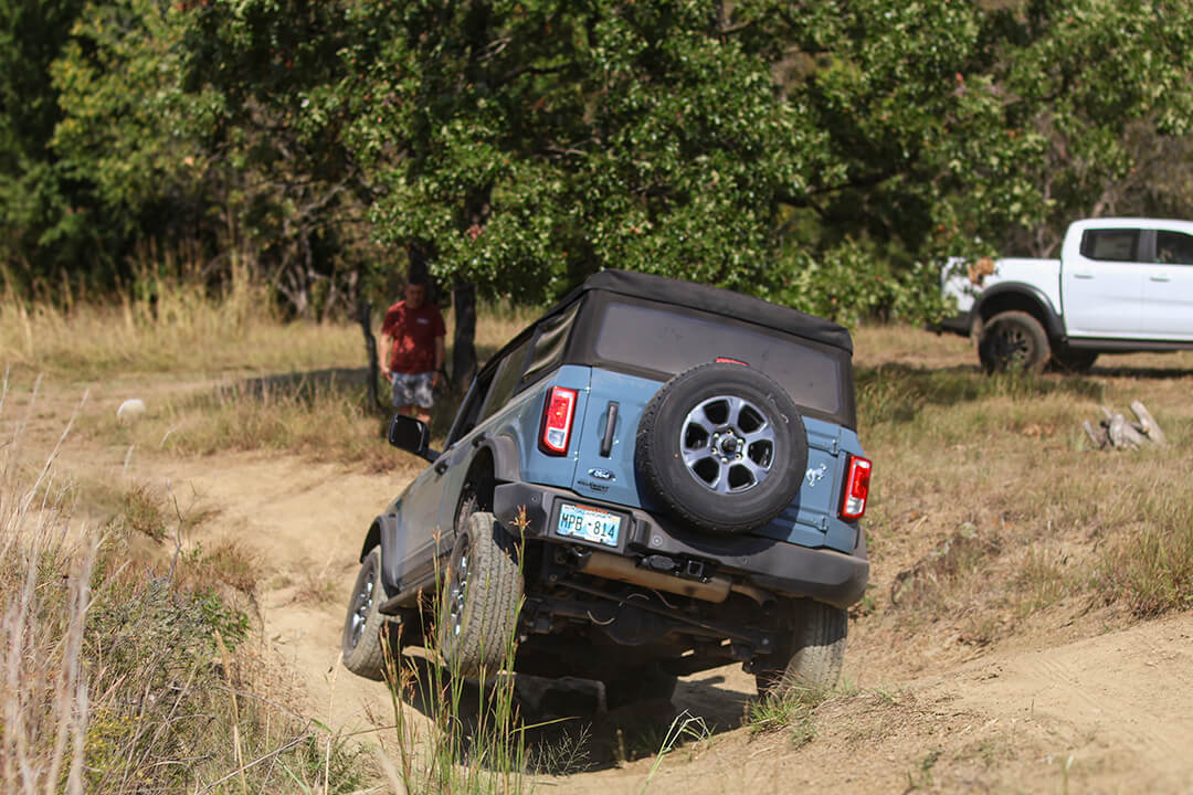 A side view of a black Ford Bronco tilted on a dirt hill.