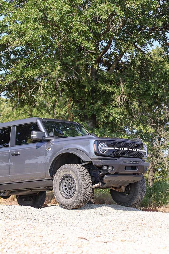 A side view of a gray Ford Bronco driving on a dirt road.
