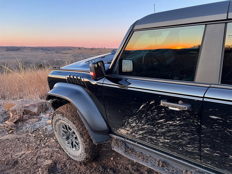 A black Ford Bronco parked on a muddy, grassy hill