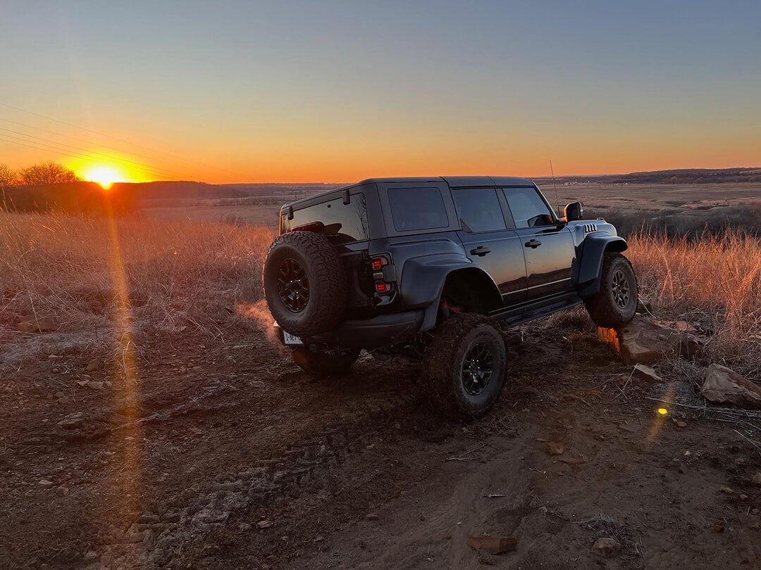 A rear view of a black Ford Bronco at sunset