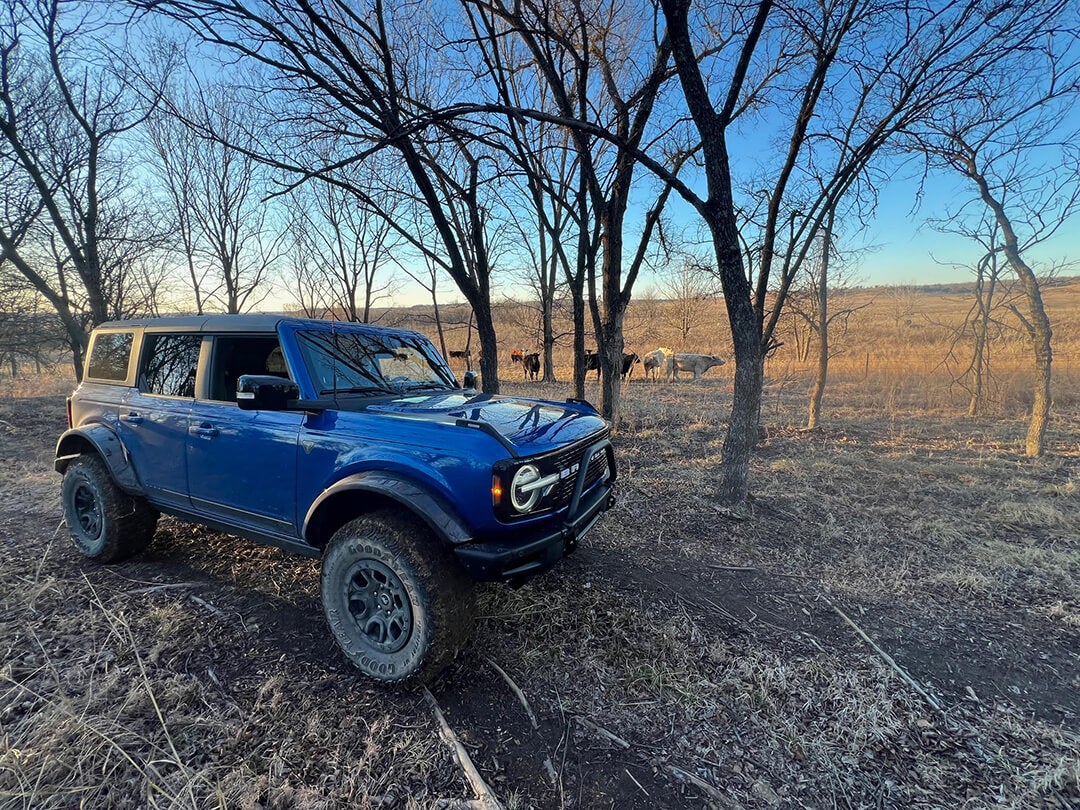A side view of a blue Ford Bronco driving on a dirt path