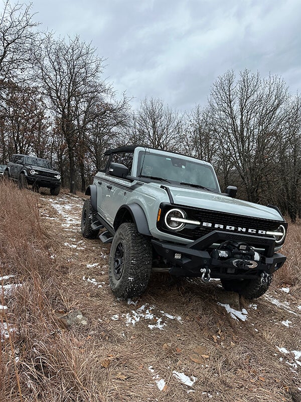 A two-door, white Ford Bronco with black stripes, off-roading