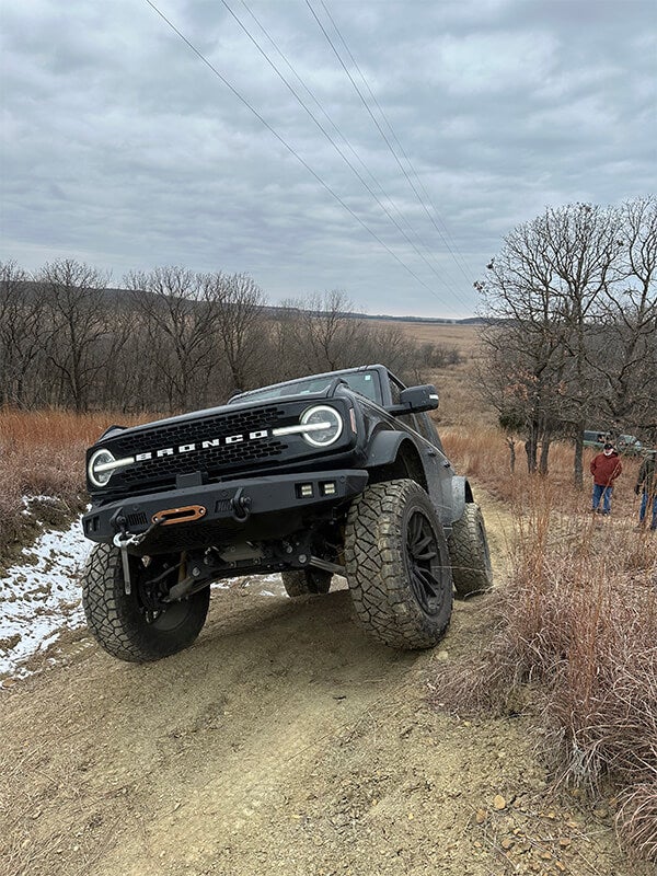 A front view of a black Ford Bronco off-roading, with big tires.