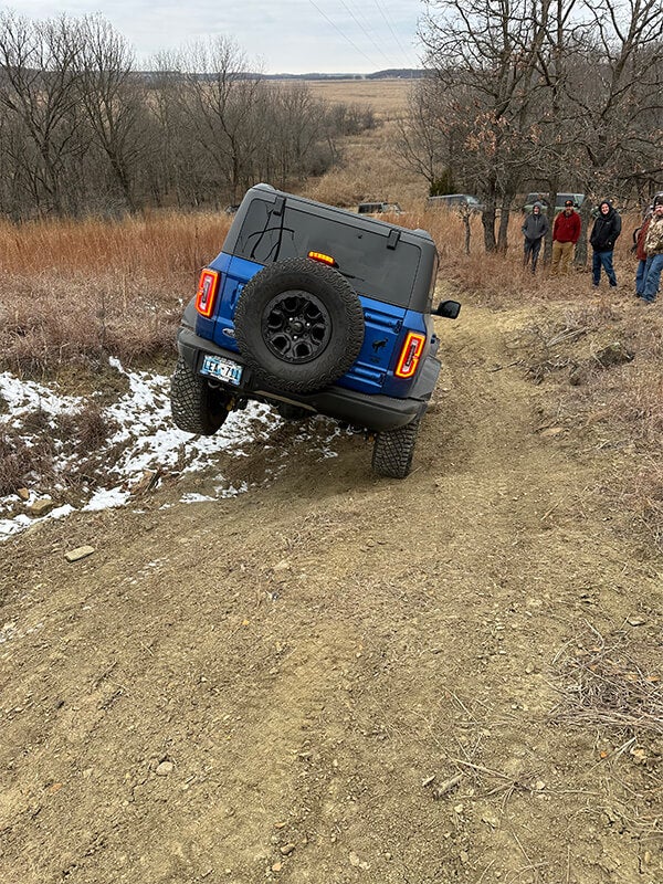 A back view of a blue Ford Bronco descending a muddy off-road trail