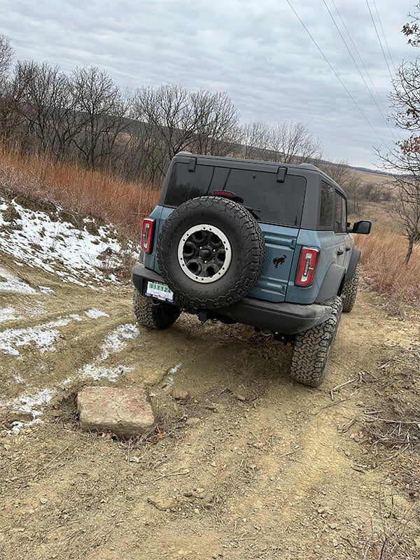 A rear view of a blue Ford Bronco descending a muddy off-road trail