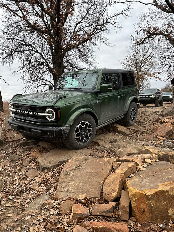 A side view of a green Ford Bronco with a black hardtop, off-roading