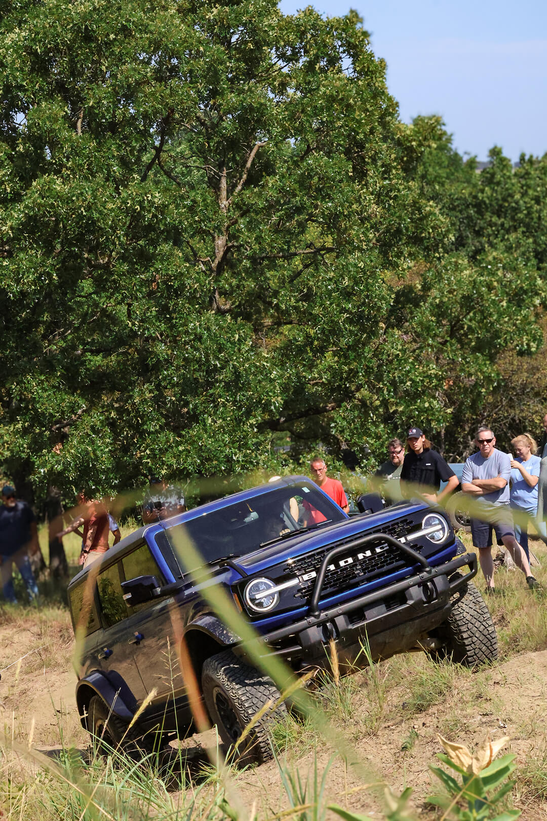A group of people watching a Ford Bronco off-road on a hill.