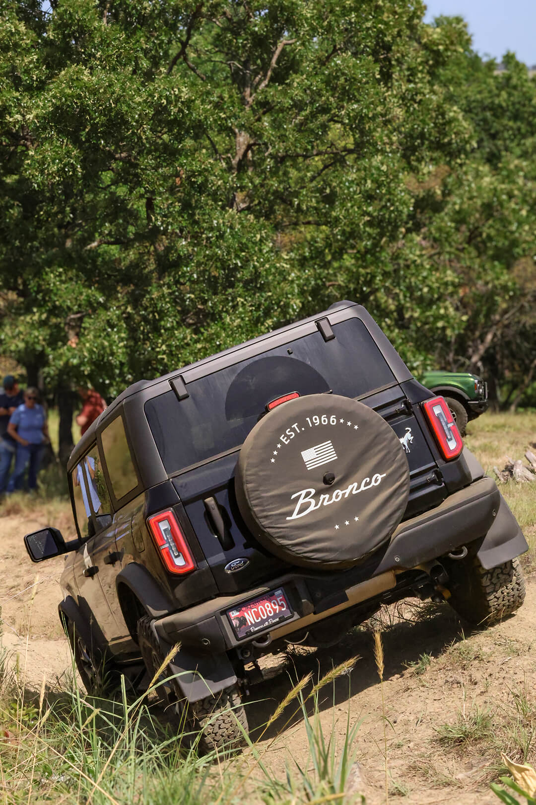 A rear view of a Ford Bronco tilted on a dirt hill