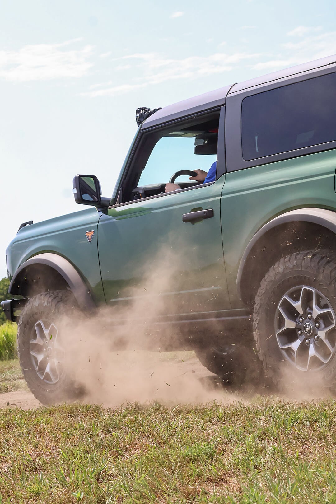 A green Ford Bronco kicking up dust on a dirt trail