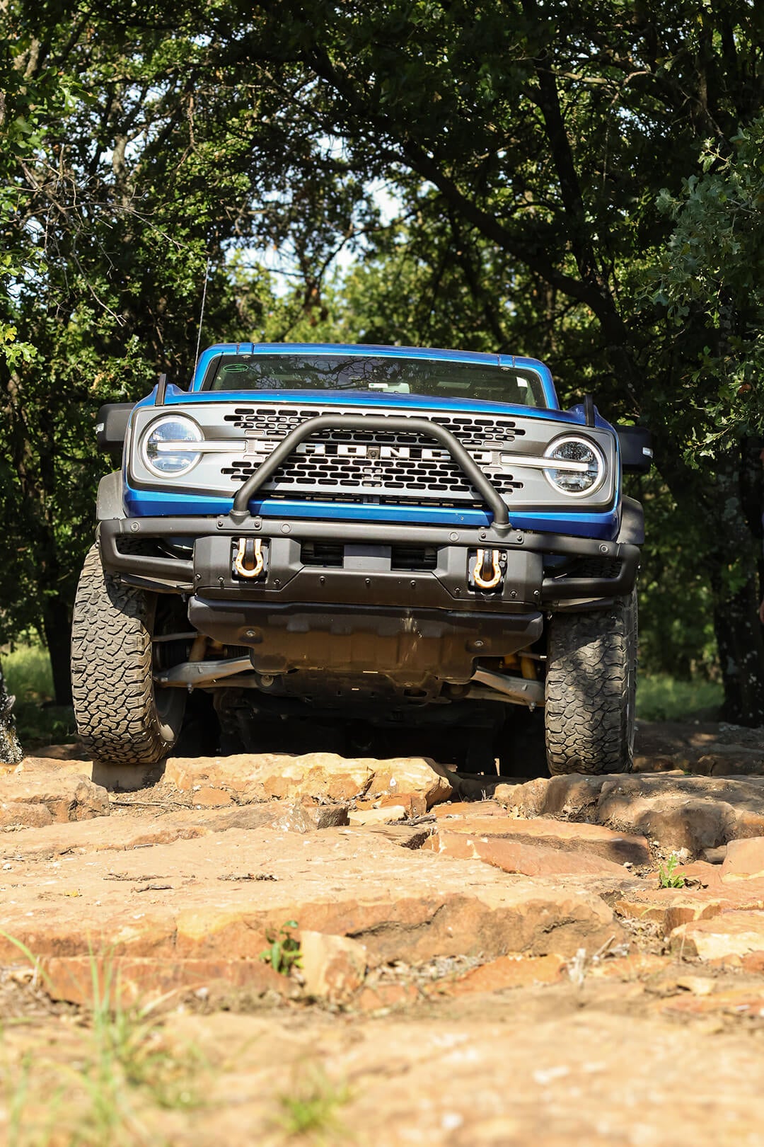 A front view of a blue Ford Bronco off-roading with an angled wheel.