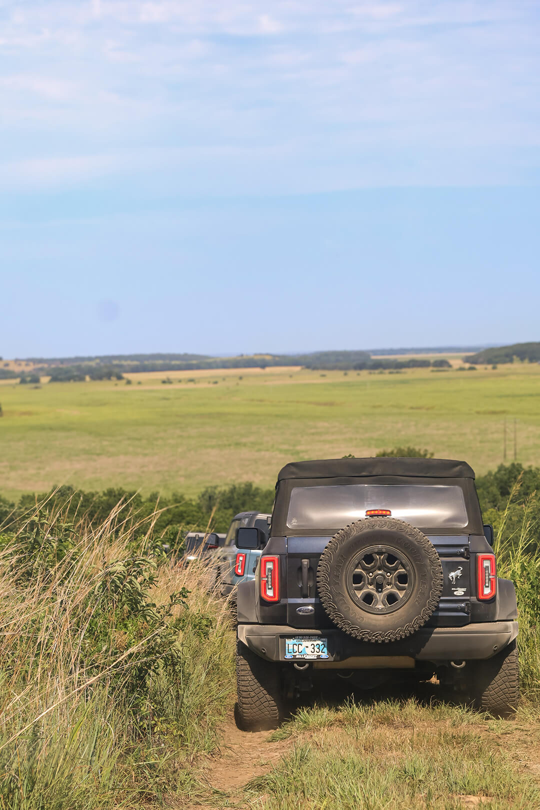 A rear view of a black Ford Bronco driving on a dirt road.